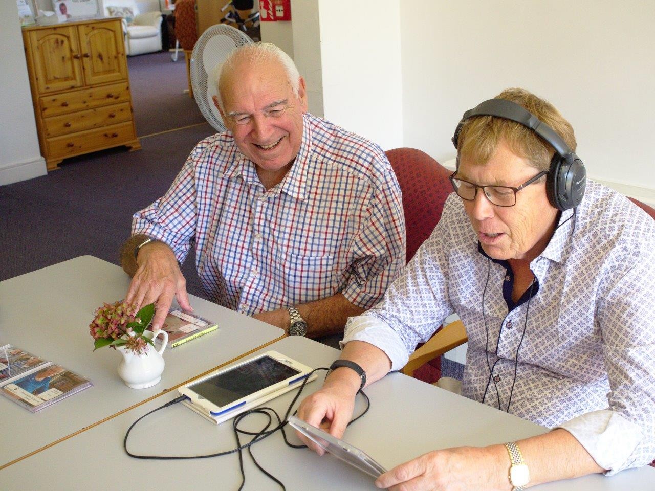Two men sitting at a table and smiling while wearing headphones.