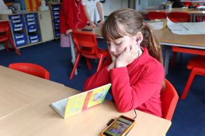 Girl sat at a school desk listening to a book on an iphone